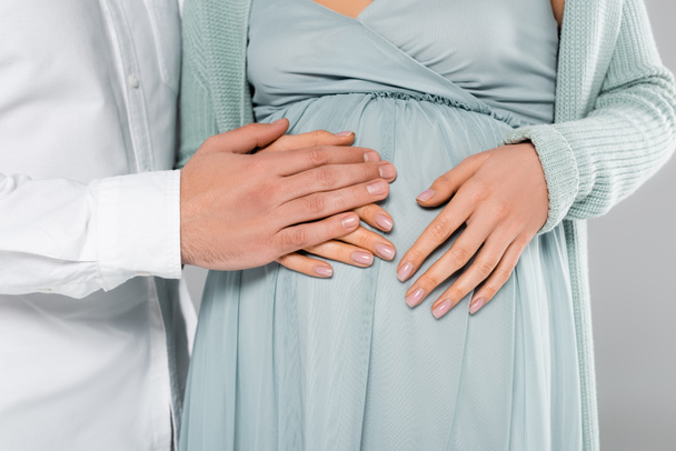 vista ritagliata dell'uomo che tiene la mano vicino al ventre della moglie incinta isolata sul grigio  - Foto, immagini