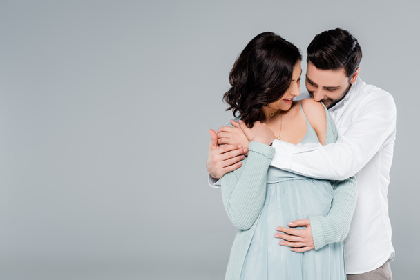 mężczyzna całowanie ramię w ciąży żona odizolowany na szary  - Zdjęcie, obraz