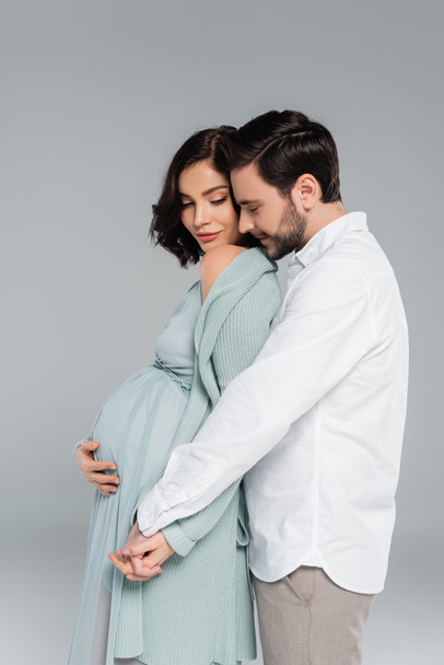 Man holding hand of pregnant wife isolated on grey  - Valokuva, kuva