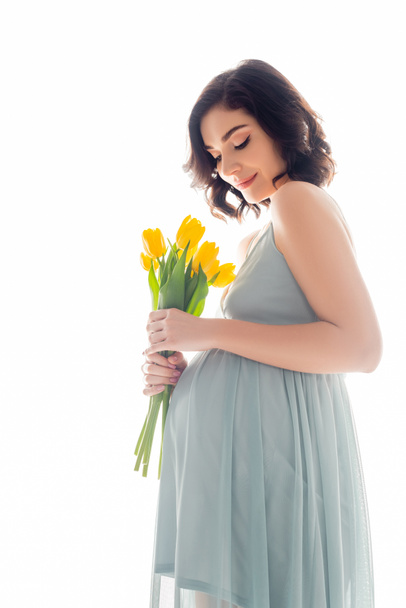 Mooie zwangere vrouw in jurk houden tulpen geïsoleerd op wit - Foto, afbeelding