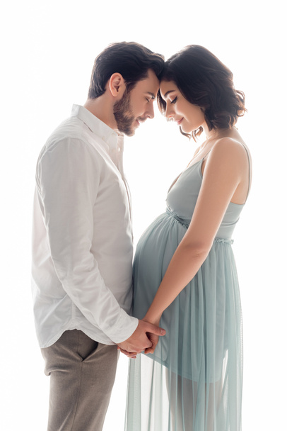 Seitenansicht einer schwangeren Frau, die die Hände ihres Mannes hält, isoliert auf weißem Grund - Foto, Bild