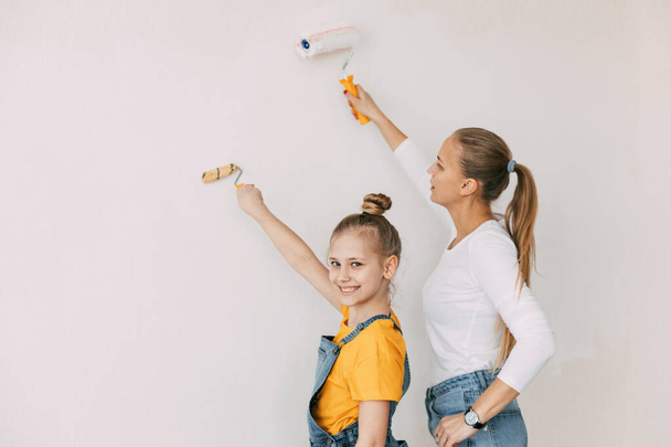 Schöne und glückliche Mutter und Tochter streichen die Wände in der Wohnung weiß - Foto, Bild