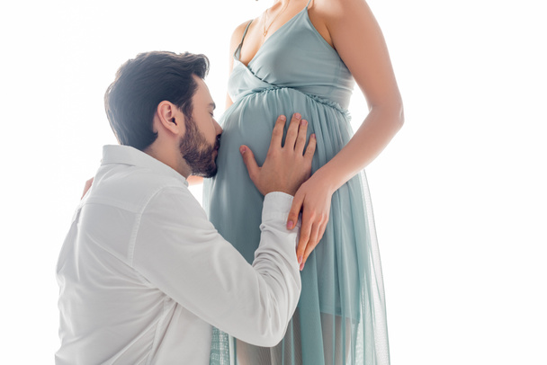 Giovane uomo baciare pancia di moglie incinta isolato su bianco - Foto, immagini