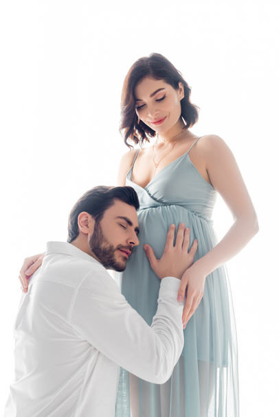 Bearded man listening belly of pregnant wife isolated on white - 写真・画像