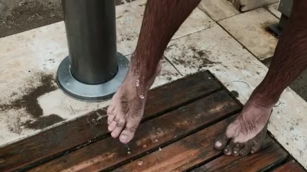 Ember mossa le a homokot a lábáról csapvízzel a strand közelében. Nyaralás szolgáltatások a tengerparton: ingyenes zuhany, hogy tisztítsa meg a lábát hosszú pihenés után a tengerparton. Turisztikai takarítás lábak nyaralás Törökországban. - Felvétel, videó