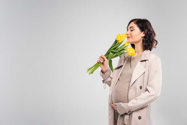 Terhes nő kabátban szagló tulipán elszigetelt szürke  - Fotó, kép