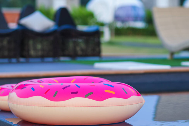 Rosa Donut-Schwimmer schwimmen auf der Oberfläche des Resortpools, um kleinen Kindern und ihren Familien beim gemeinsamen Spielen zu helfen. Der Pool in der Villa hat einen rosafarbenen Gummiring für die Kunden vorbereitet. - Foto, Bild