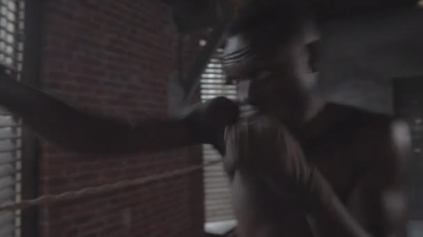Waist-up-Aufnahme eines entschlossenen jungen afroamerikanischen Kämpfers mit nackter Brust im Schattenboxen in einem grotesken Industriegebäude und praktizierenden Schlägen, Schlägen und Haken - Filmmaterial, Video