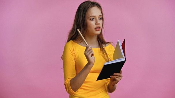 pensativo adolescente sosteniendo portátil y pluma aislado en rosa  - Foto, Imagen