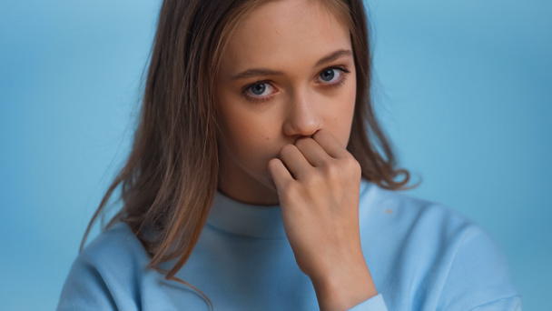 беспокойная девочка-подросток в толстовке смотрит на камеру изолированную на голубом - Фото, изображение