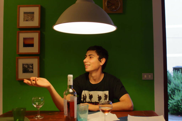 un chico italiano gesticula mientras habla con sus amigos en una mesa bebiendo vino - Foto, imagen