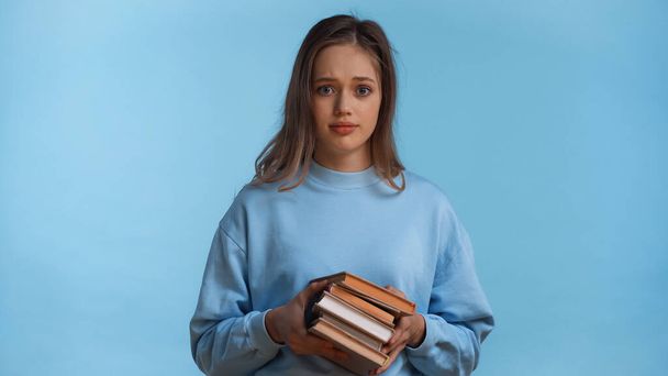 adolescente en sudadera sosteniendo libros aislados en azul - Foto, imagen