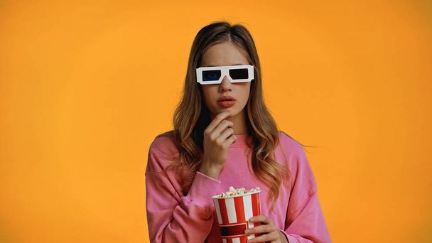 tini lány 3D-s szemüveg gazdaság vödör és eszik popcorn izolált sárga - Fotó, kép