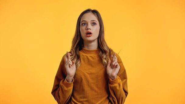 adolescente em suéter com dedos cruzados e boca aberta isolada em amarelo - Foto, Imagem