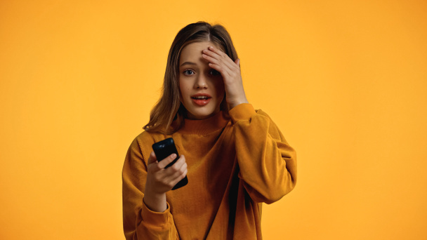 amazed teenager in sweater holding remote controller isolated on yellow - Foto, Imagen