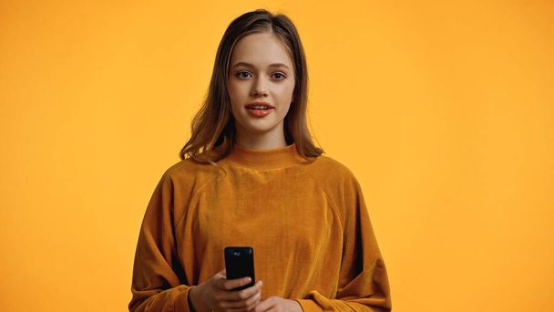 happy teenager in sweater holding remote controller isolated on yellow - Photo, Image
