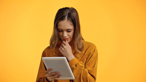adolescente pensativo en suéter mirando tableta digital aislado en amarillo - Foto, Imagen