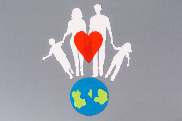 Jour de la Terre. Un symbole feutré de la planète Terre et un cœur rouge avec une silhouette en papier de la famille. Fond gris. Pose plate. Espace de copie. Le concept de protection de l'environnement. - Photo, image