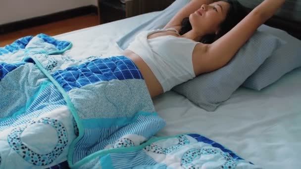 Зав'язаний постріл молодої красивої азіатської жінки в сонний одяг лежить в ліжку, дивлячись задумливо і розтягуючи себе після пробудження  - Кадри, відео