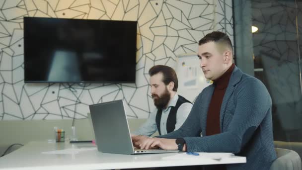 Una imagen de dos programadores trabajando en un portátil y una tableta. Programadores web en trabajo remoto. Los hombres miran a la cámara. - Metraje, vídeo