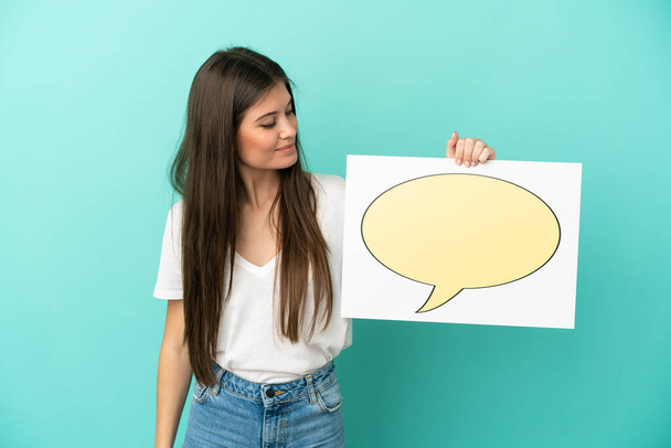 Young caucasian woman isolated on blue background holding a placard with speech bubble icon - Photo, Image
