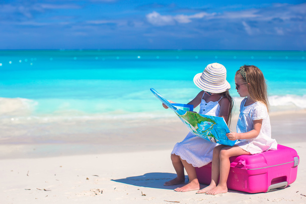 Niñas lindas con una maleta grande y un mapa en la playa tropical
 - Foto, Imagen