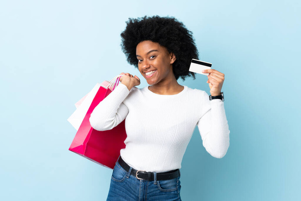 Young African American woman isolated on blue background holding shopping bags and a credit card - Fotografie, Obrázek