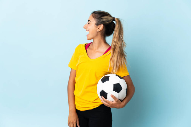 Joven futbolista hispana mujer aislada sobre fondo azul riendo en posición lateral - Foto, Imagen