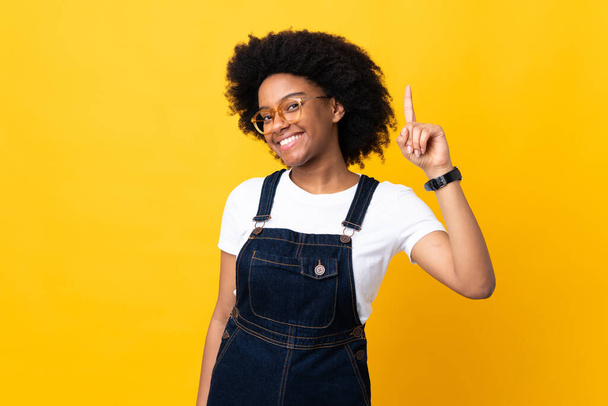 Giovane donna afroamericana isolata su sfondo giallo mostrando e alzando un dito in segno del meglio - Foto, immagini