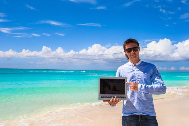 Young man with laptop on the background of turquoise ocean at tropical beach - Photo, Image