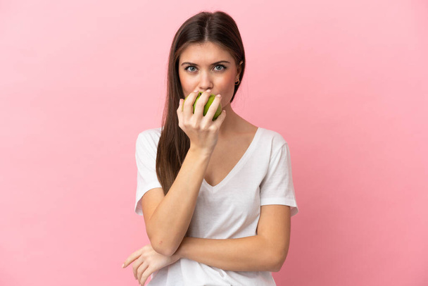 ピンクの背景に孤立した若い白人女性がリンゴを食べる - 写真・画像