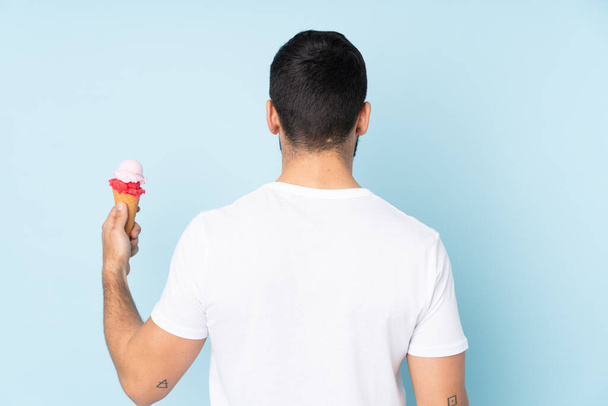 背部の位置に青の背景に隔離されたコーンアイスクリームを持つ白人男性 - 写真・画像