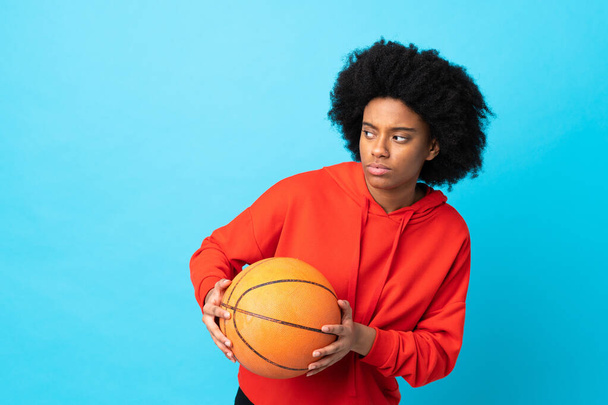 若いアフリカ系アメリカ人の女性はバスケットボールをプレイ青い背景に隔離 - 写真・画像