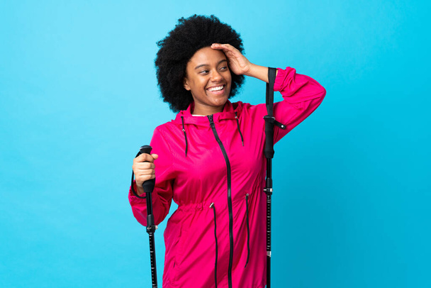 Young Africa American with backpack and trekking poles isolated on blue background smiling a lot - Photo, image