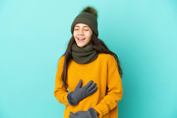 Fiatal francia lány elszigetelt kék háttér téli kalap mosolygott sokat - Fotó, kép