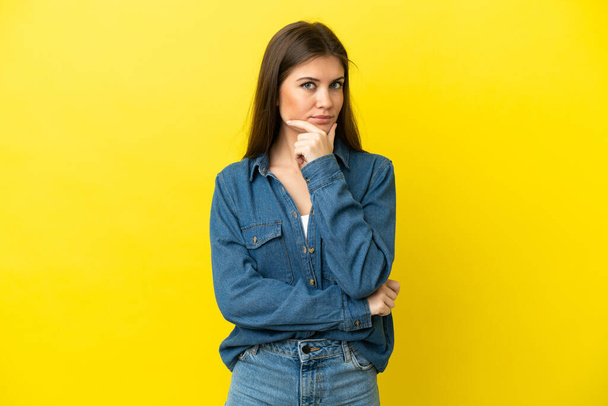 Молода біла жінка ізольована на жовтому тлі думаючи про ідею під час пошуку
 - Фото, зображення