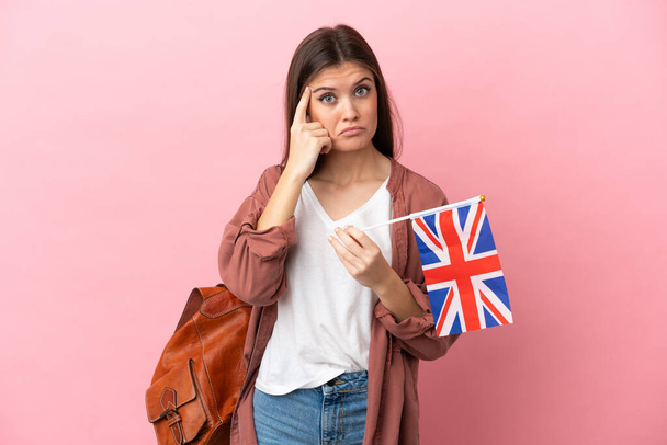 ピンクを背景にイギリス国旗を掲げた若い白人女性がアイデアを思いつく - 写真・画像