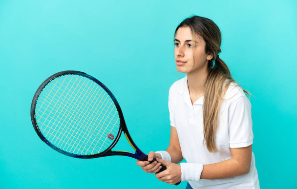 Mavi arka planda izole edilmiş genç beyaz kadın tenis oynuyor. - Fotoğraf, Görsel