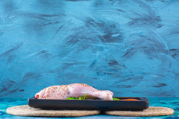 Bacchetta di pollo cruda marinata con pomodori in un piatto di legno sul rivetto, sullo sfondo blu. Foto di alta qualità - Foto, immagini