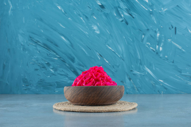 Chopped red fermented sauerkraut in a bowl on a trivet , on the blue background. High quality photo - Photo, Image