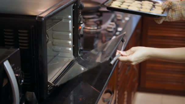 Mulher irreconhecível usando luva de forno colocando assadeira com cortar biscoitos em forno pré-aquecido na cozinha doméstica - Filmagem, Vídeo