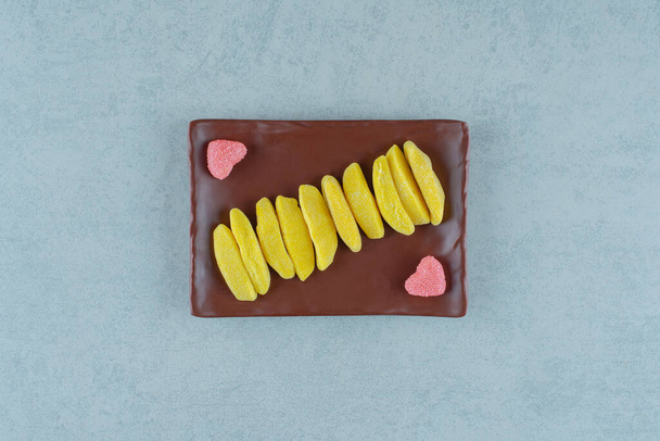 Un plato marrón de caramelos de mascar en forma de plátano con mermeladas azucaradas en forma de corazón. Foto de alta calidad - Foto, imagen
