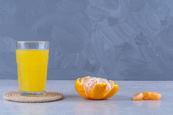 Een glas sinaasappel sappig op een trivet naast gesneden mandarijn, op de marmeren achtergrond. Hoge kwaliteit foto - Foto, afbeelding