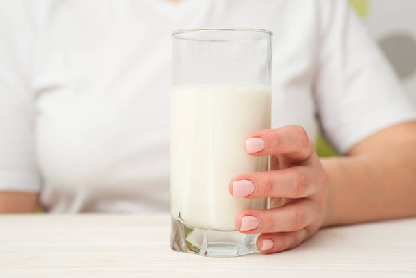 La donna con un bicchiere di latte siede a un tavolo di legno bianco. Note di alimentazione. Stile di vita sano. - Foto, immagini