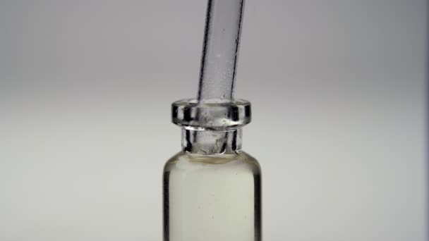 O close-up de uma pipeta vazia que está sendo trazida para um frasco de vidro e líquido é retirado de lá, isolado em fundo cinza. Conceito de medicina e óleos - Filmagem, Vídeo
