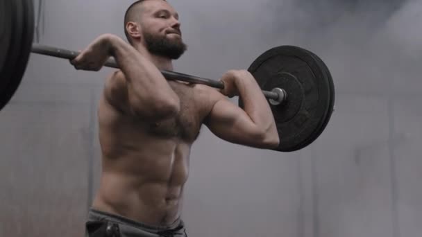 Mittlere Aufnahme eines muskulösen kaukasischen sportlichen Mannes mit nacktem Oberkörper beim Kniebeugen mit schwerer Langhantel im Fitnessstudio - Filmmaterial, Video