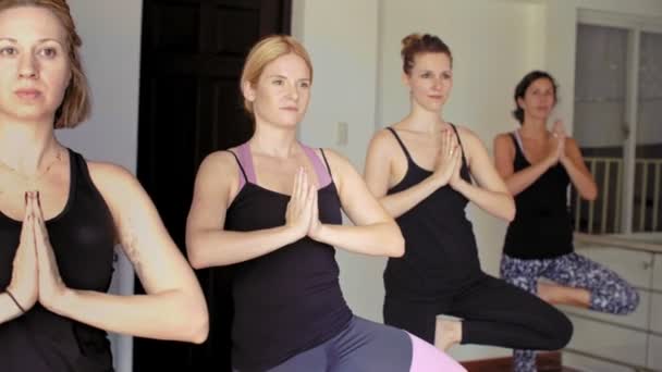 Cuatro jóvenes mujeres caucásicas en ropa deportiva practicando la pose de árbol mientras toman clases de yoga en el estudio - Imágenes, Vídeo