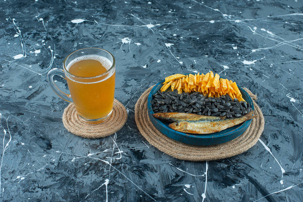 Un bicchiere di birra e antipasti sul piatto di legno sul rivetto, sullo sfondo blu. Foto di alta qualità - Foto, immagini