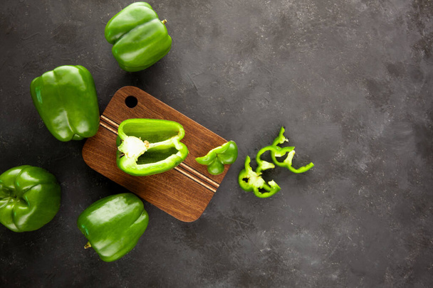 Sweetn groene paprika 's op houten snijplank op zwarte en donkergrijze achtergrond. Groene peper gesneden en gehakt op houten snijplank. Groene paprika 's. - Foto, afbeelding