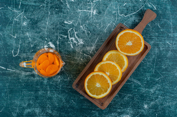 Спелый ломтик апельсина на доске, рядом с соком в графине на мраморном фоне. Высокое качество фото - Фото, изображение
